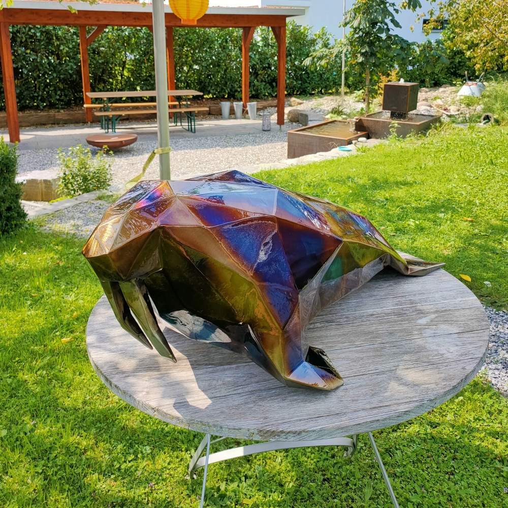 Glossy polygonal seal sculpture made of welded metal, resting on a wooden surface